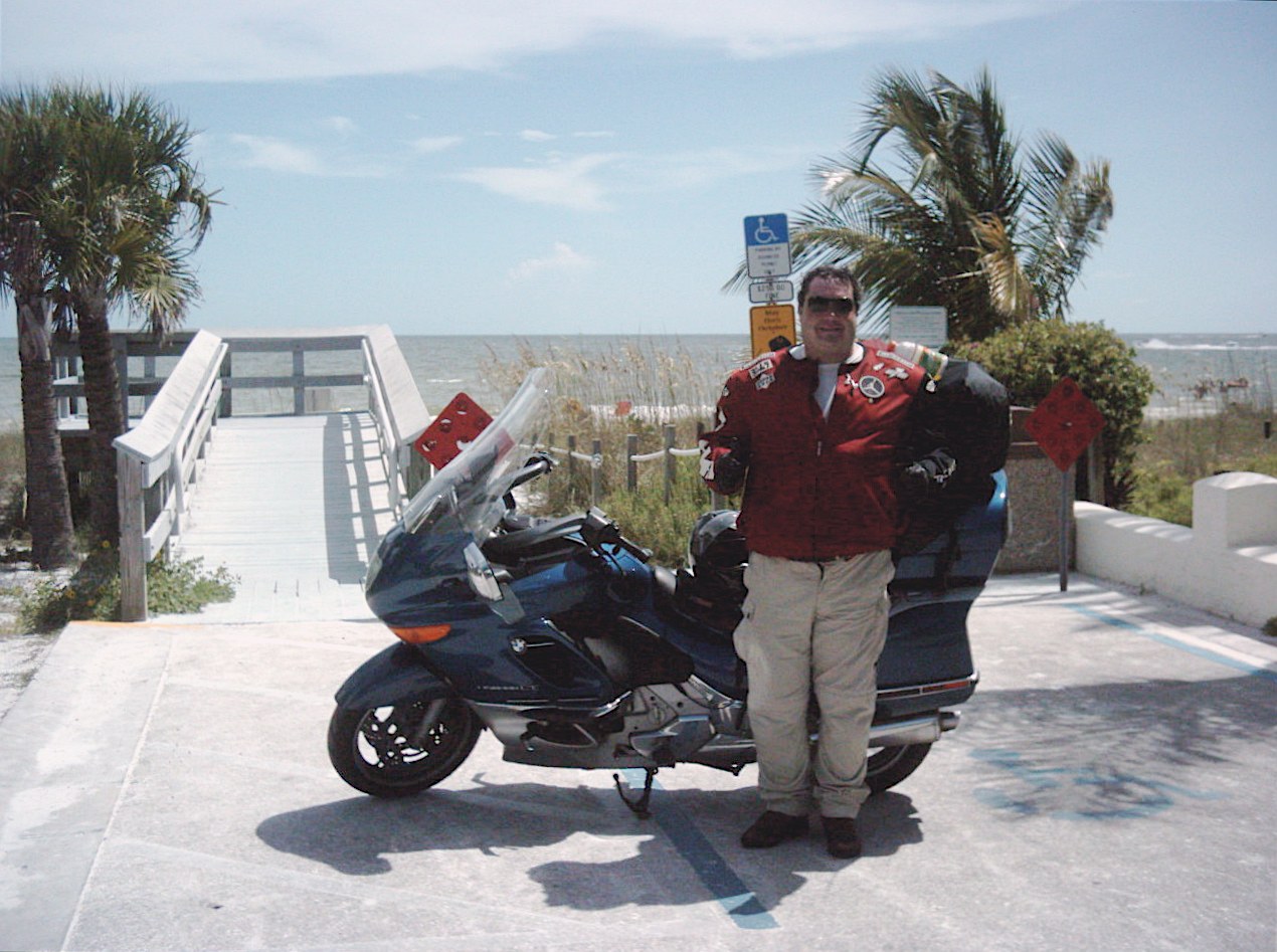 John standing with fully loaded Grace at a Florida beach boardwalk under palm trees
